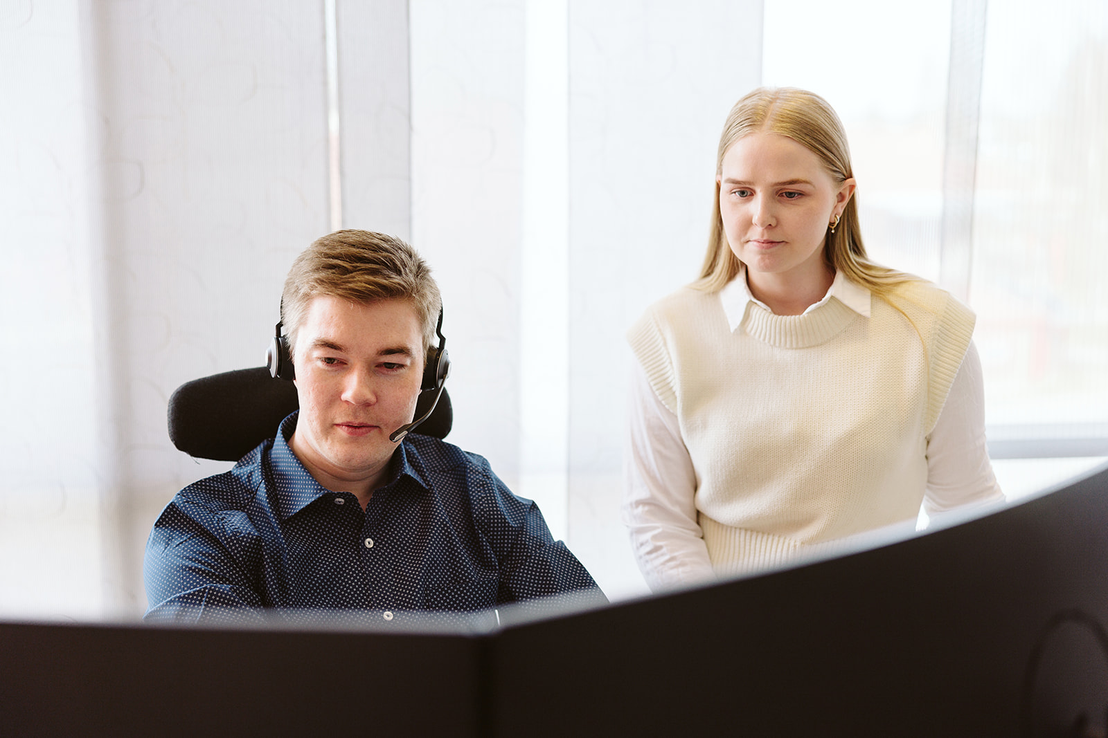 Ansatte i Norsis jobber i åpent landskap. Mann med headsett sitter foran PC mens en annen kvinne står ved siden av.