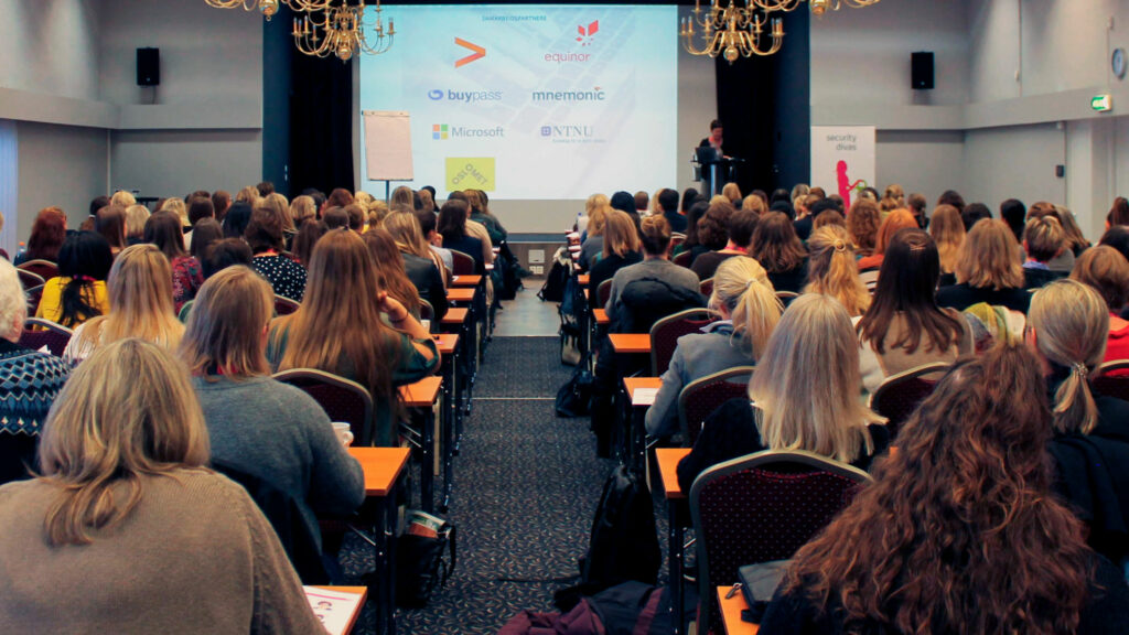 bilde fra security divas konferansen 2022 - bakhodene til mange kvinner ser opp på presentasjon